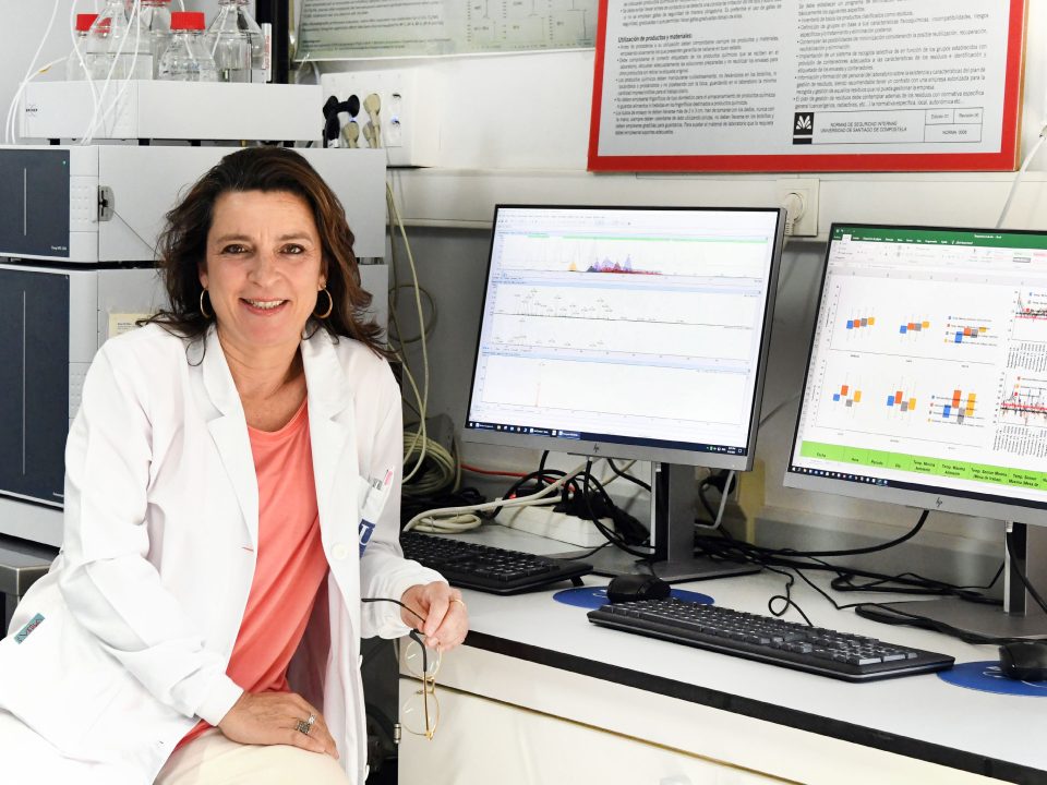Marta Lores sitting in her lab with two computer screens.